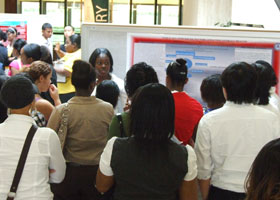 Photo of students crowding around Dajia Shields as she presents her research on health-related stresses on Puerto Rican women